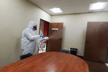 A worker for My Angel Maids sprays disinfectant on a boardroom