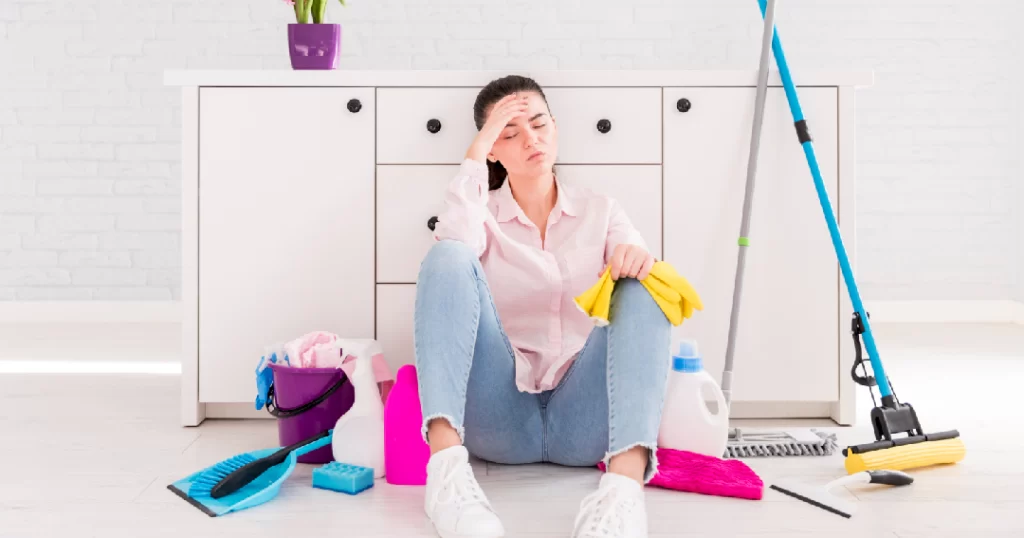 Tired woman sitting on the floor surrounded by home cleaning supplies